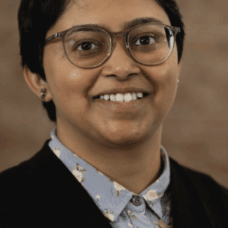 Vasundhara Kamath smiling at the camera against a brown background.